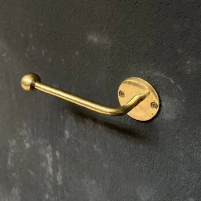 Handmade unlacquered brass toilet paper holder mounted on a modern white tiled bathroom wall.